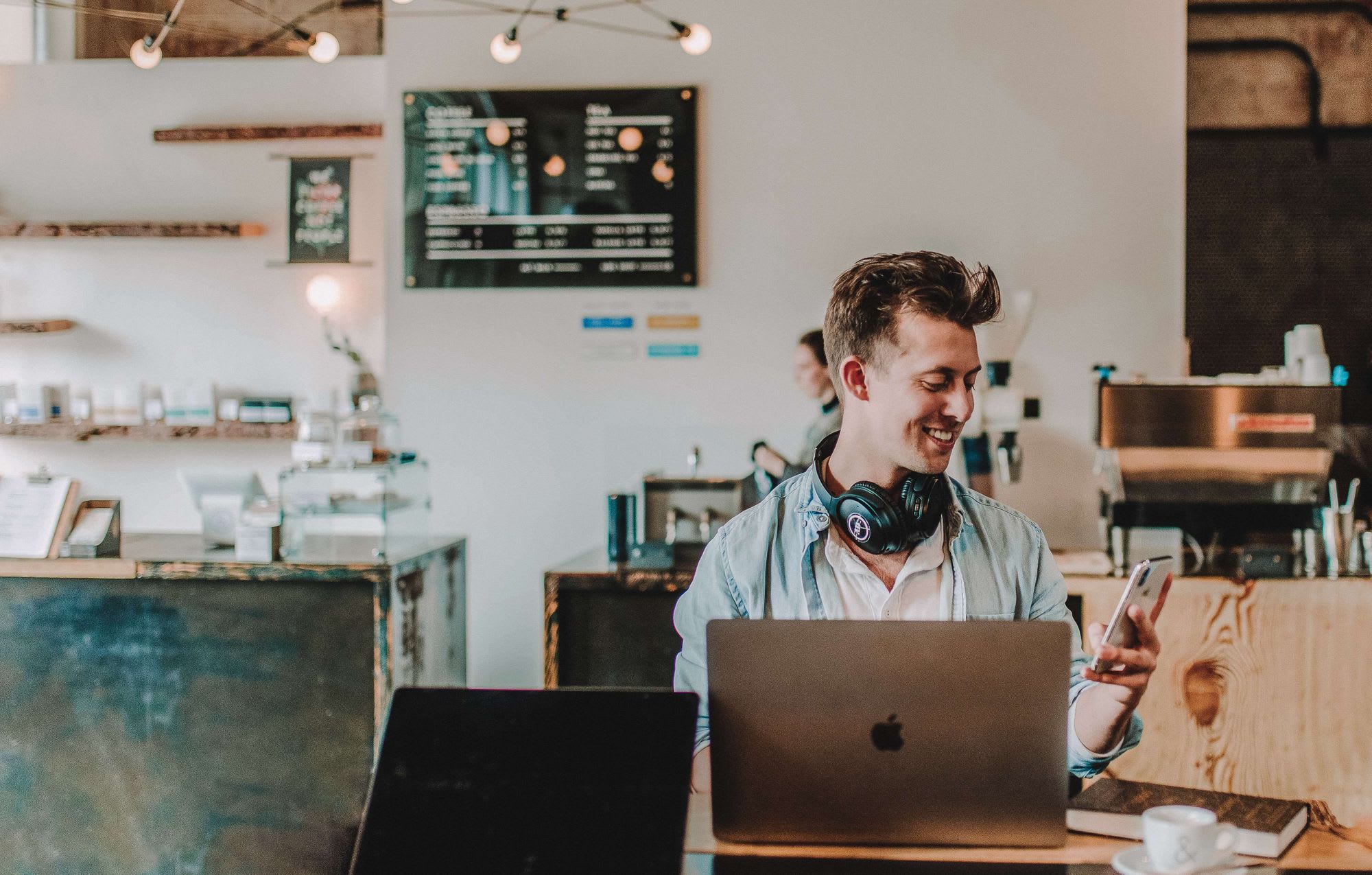 Man sitting with laptop looking at his phone smiling